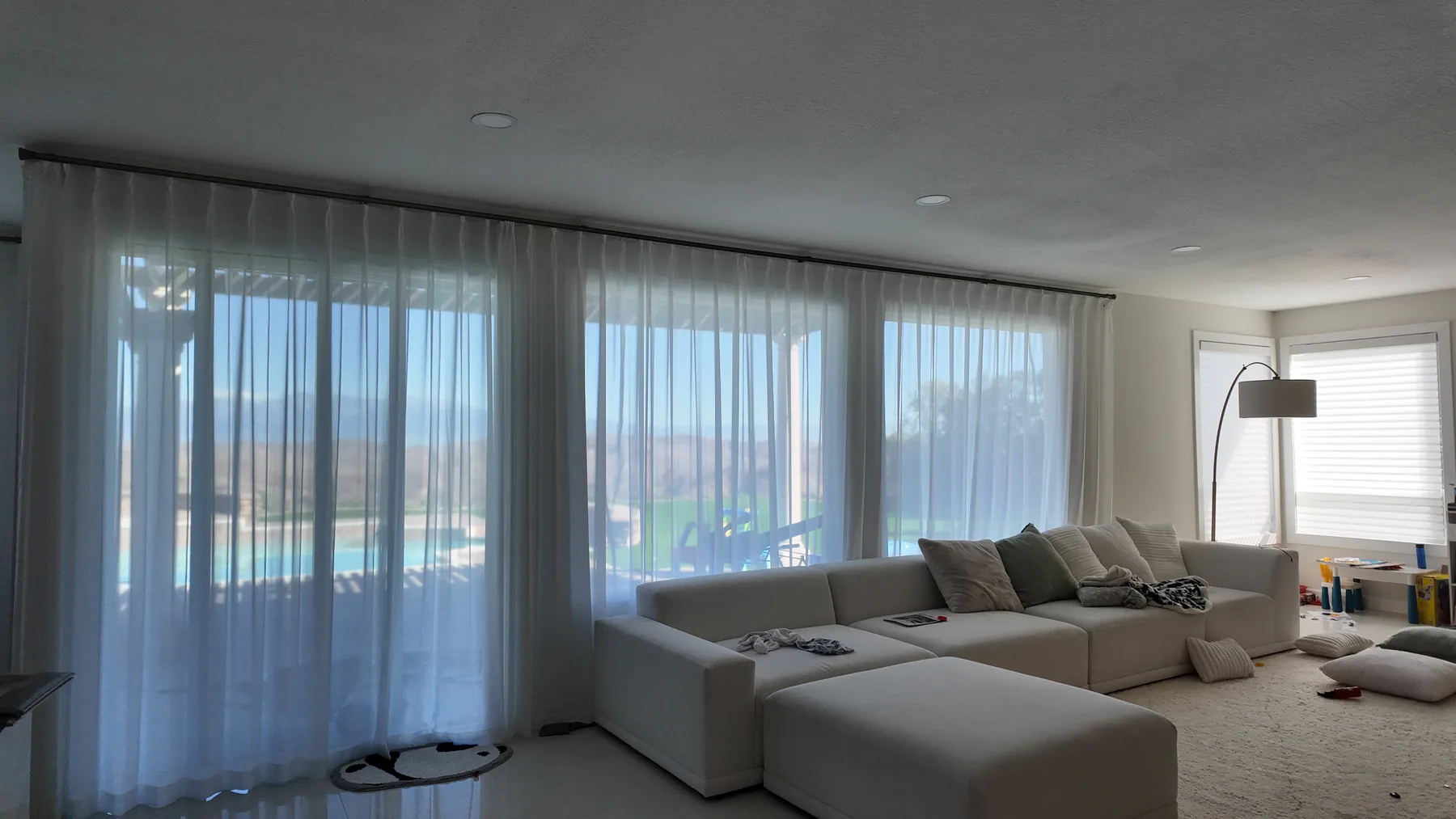 Sheer curtains installed across living room windows behind a sectional sofa.