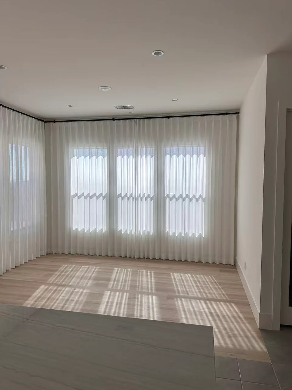 Sheer curtains installed below high transom windows in a tall room.