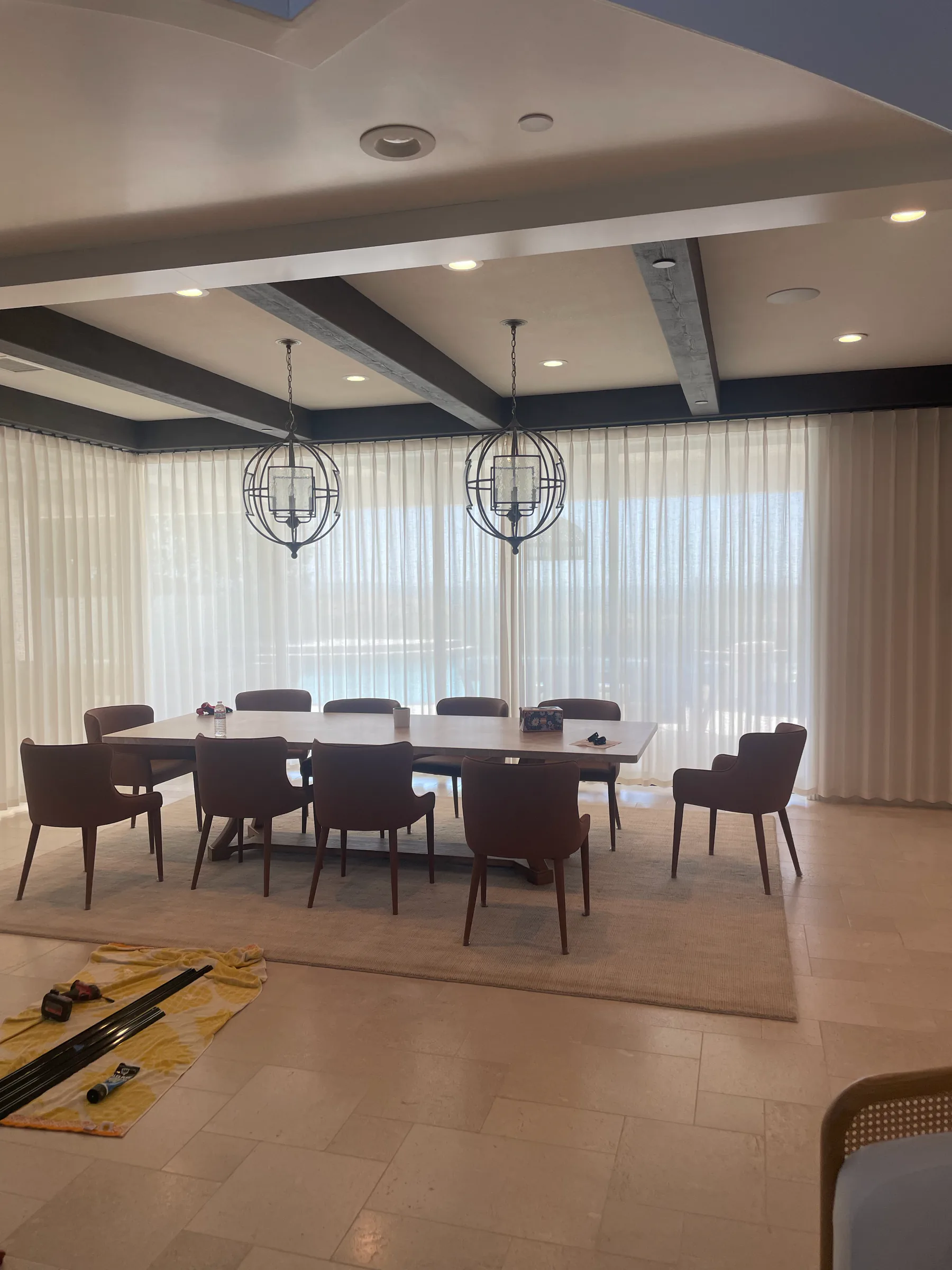 Sheer curtains installed along a dining room wall with large windows.
