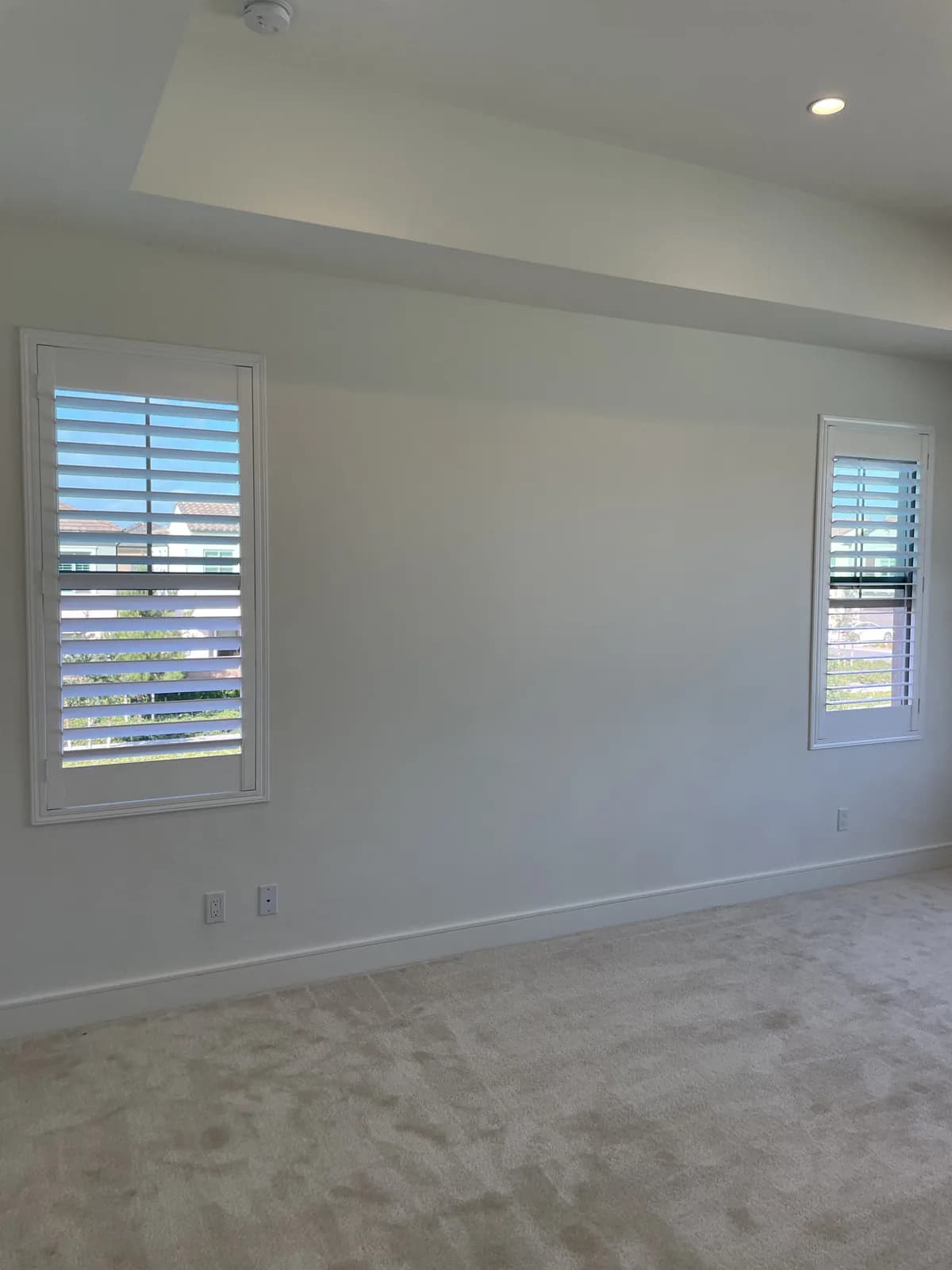 Two narrow windows with white plantation shutters in a carpeted bedroom