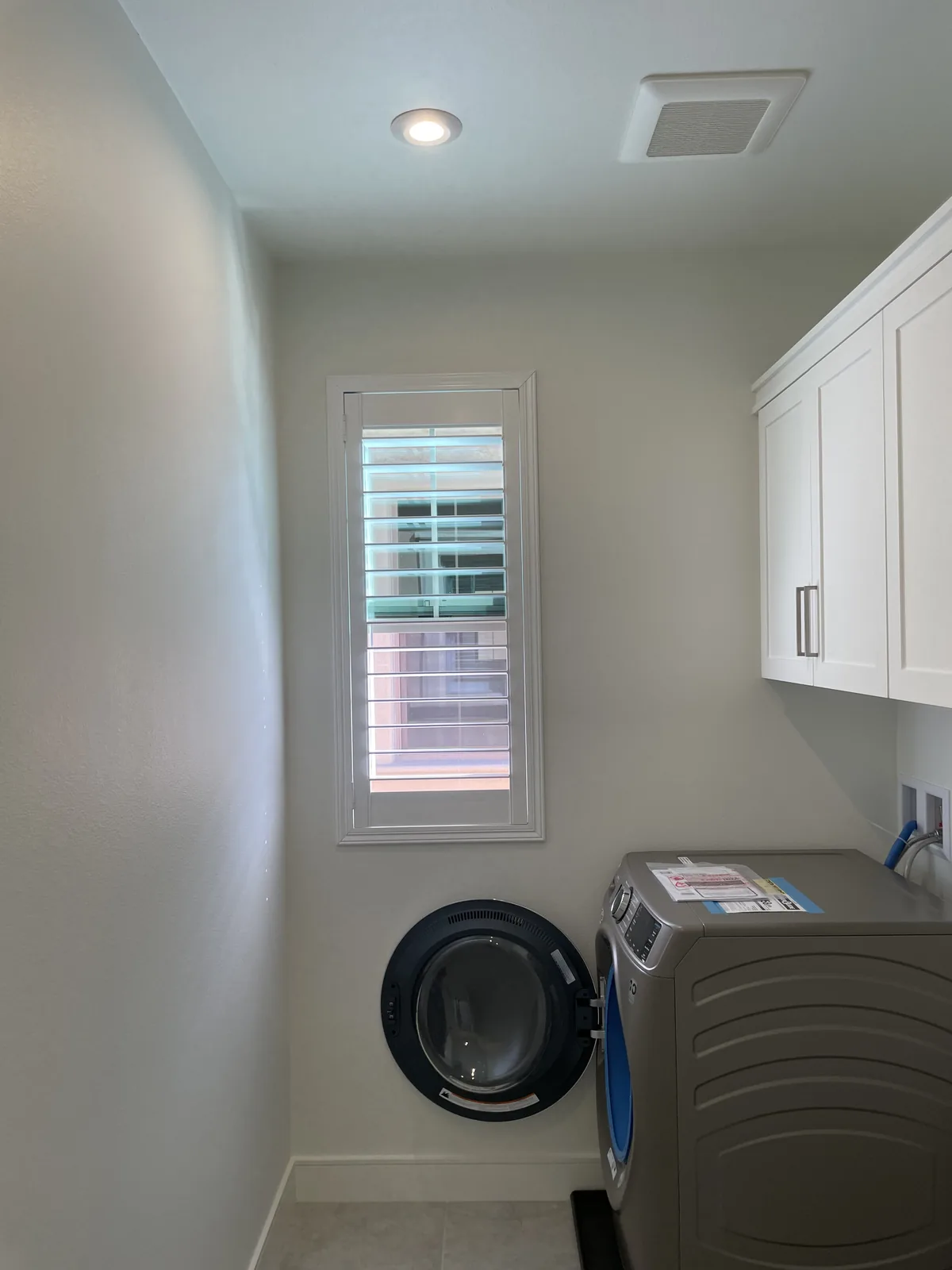 White plantation shutter on a narrow window beside a washer and dryer