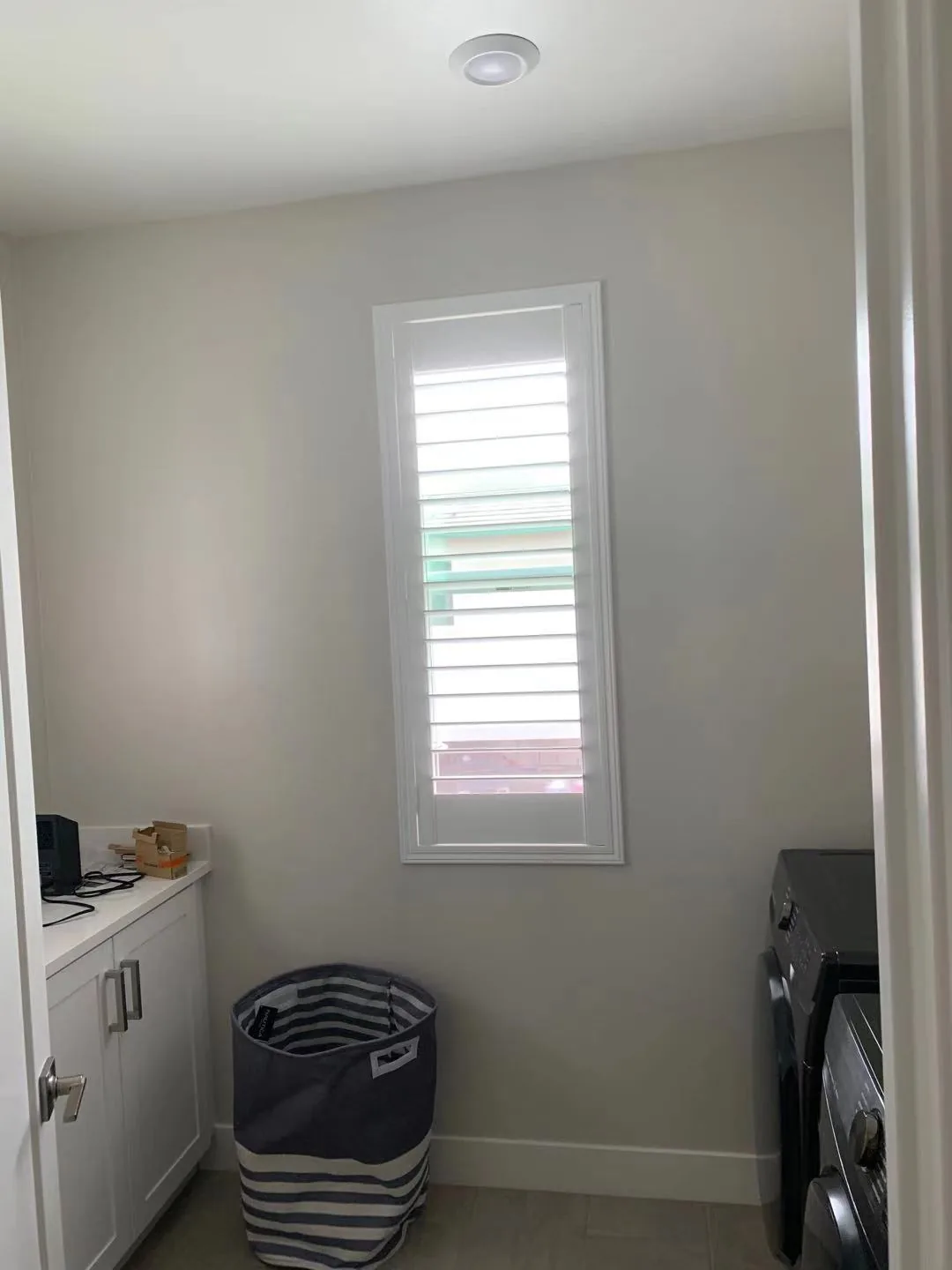 White plantation shutter on a narrow laundry-room window beside cabinetry