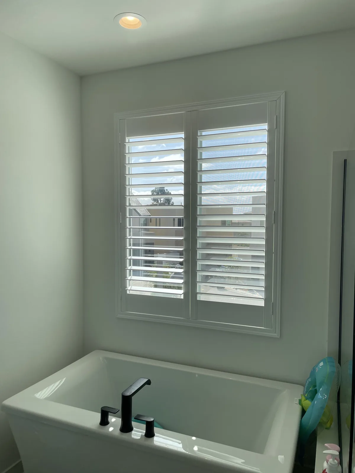 White plantation shutters on paired windows above a bathtub in Portola Springs, Irvine