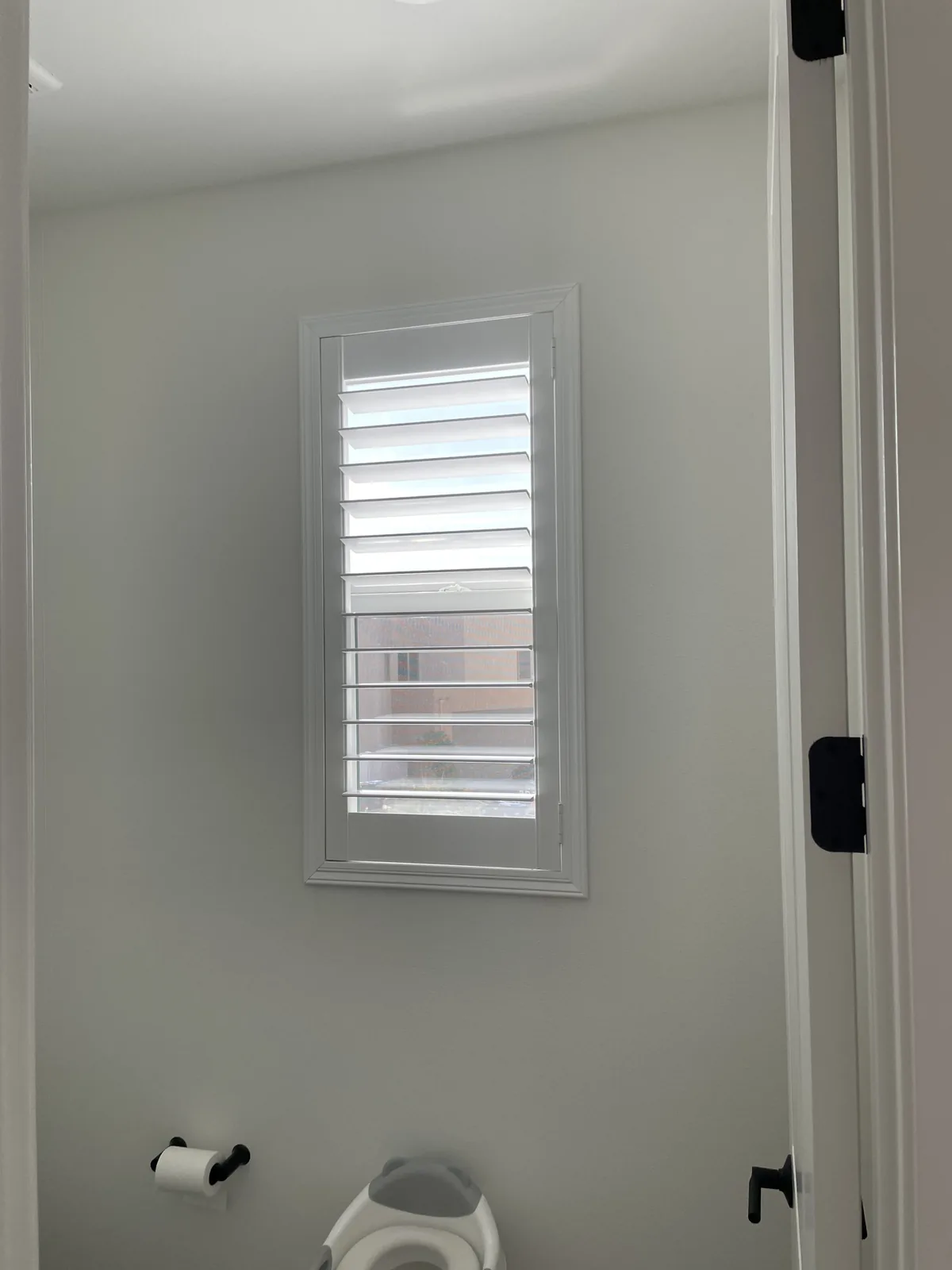 White plantation shutter on a small bathroom window beside the toilet