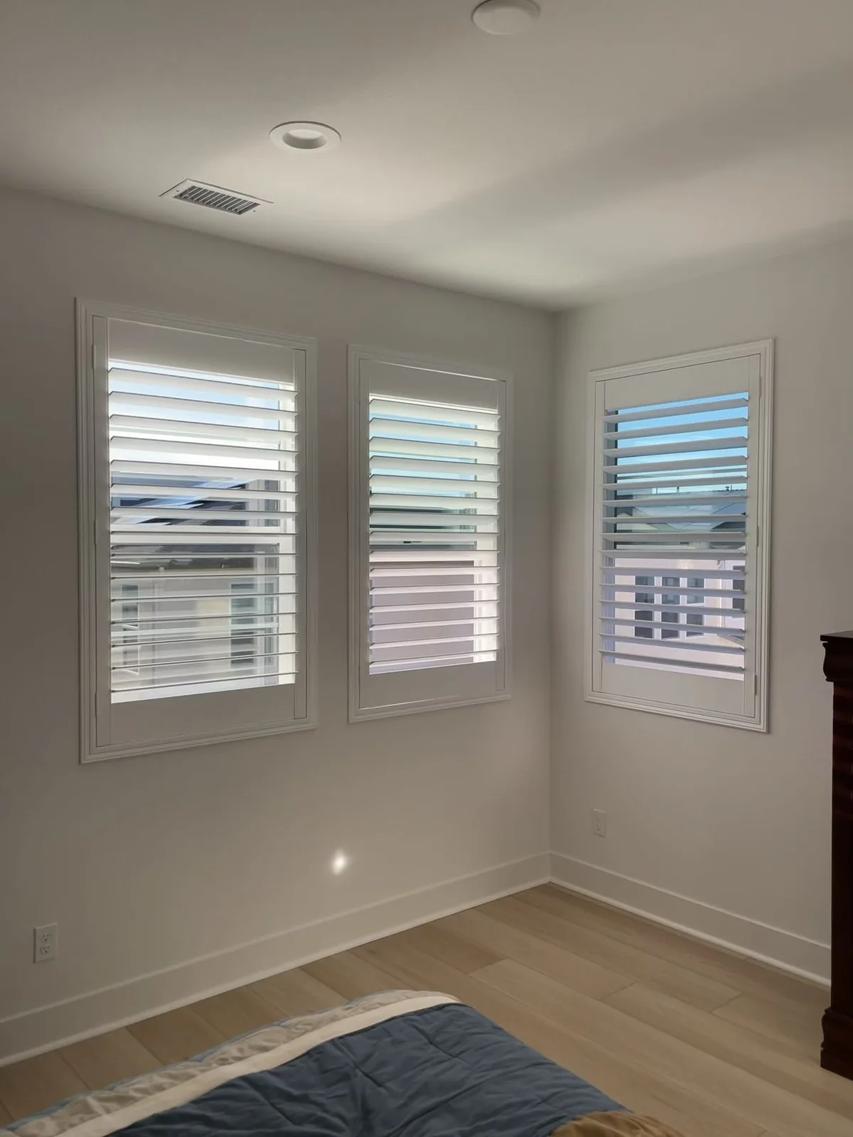 White plantation shutters on grouped windows around a bedroom corner