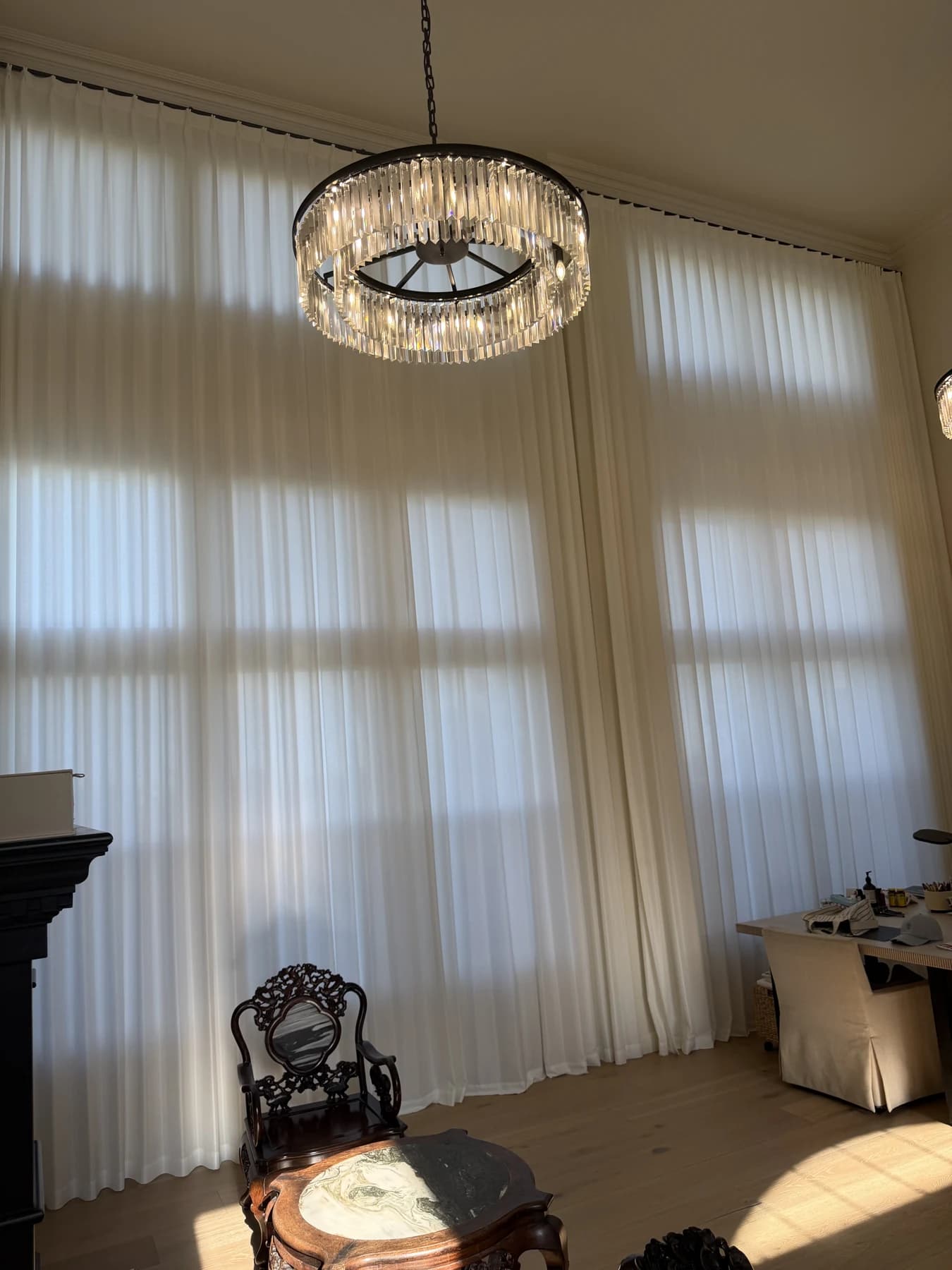 Light-colored floor-to-ceiling sheer curtains across tall windows beside a chandelier in a Newport Beach home