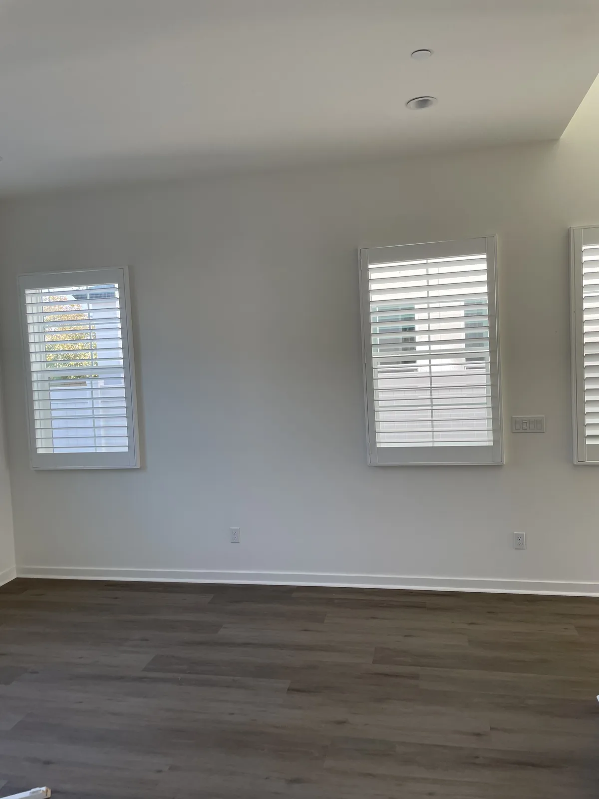 White plantation shutters across separate windows on a living-area wall in Rancho Cucamonga