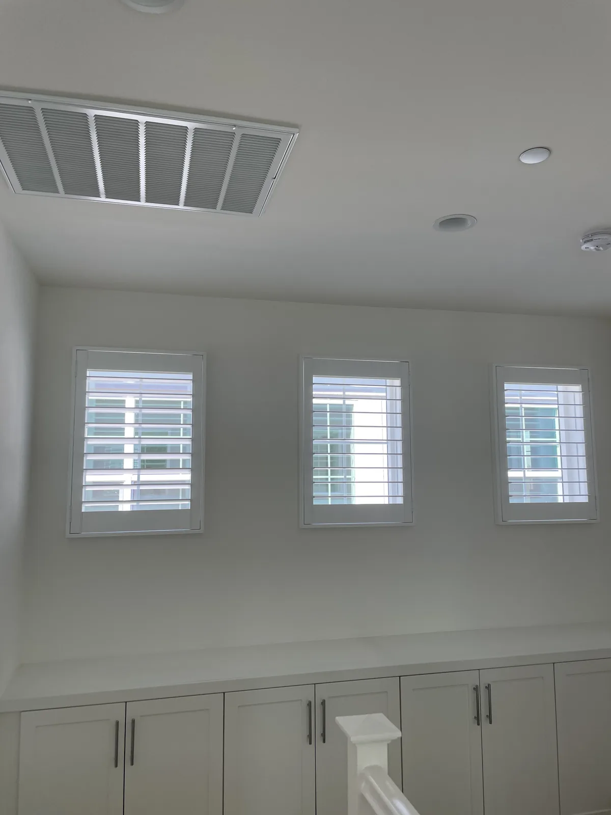 Three white plantation shutters above built-in lower cabinets